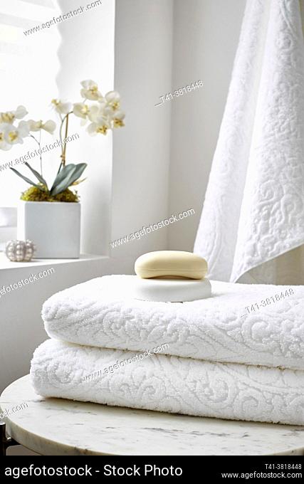 A stack of white towels in a spa setting with soap and an orchid