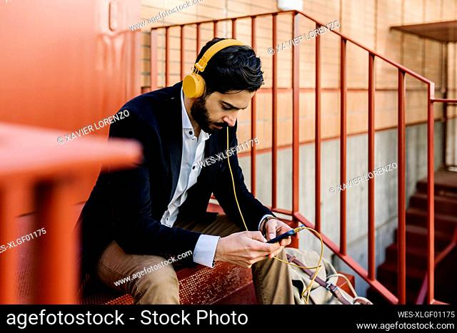 Businessman wearing headphones using mobile phone while sitting on steps