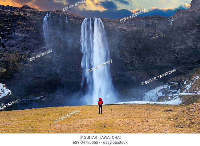 Seljalandsfoss waterfall in Iceland. Guy in red jacket looks at Seljalandsfoss waterfall