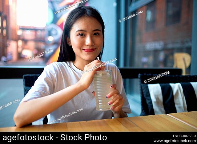 Asian young woman drink lemonade soda at the outdoors cafe and smiles