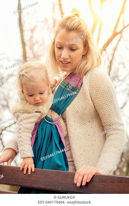 Portrait of a mother carrying her little baby in a baby carrier scurf in the park