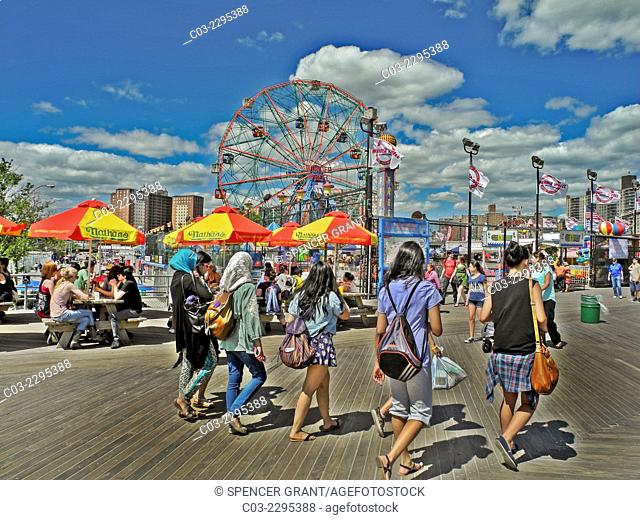 Young women enjoy a sunny day on the boardwalk at Coney Island, New York City. Note umbrellas from the famous Nathan's restaurant, Muslim head scarfs