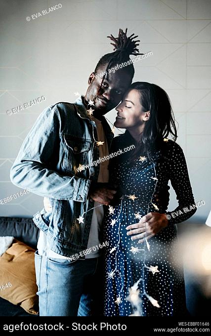 Young man and smiling pregnant woman with star shaped lights at home