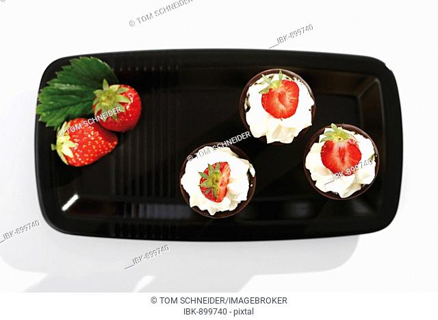 Three wafer cones with cream and strawberries on a black tray