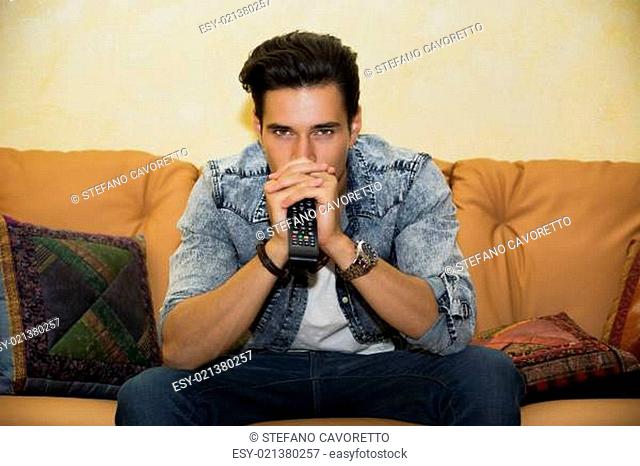 Young man sitting watching television changing the channel
