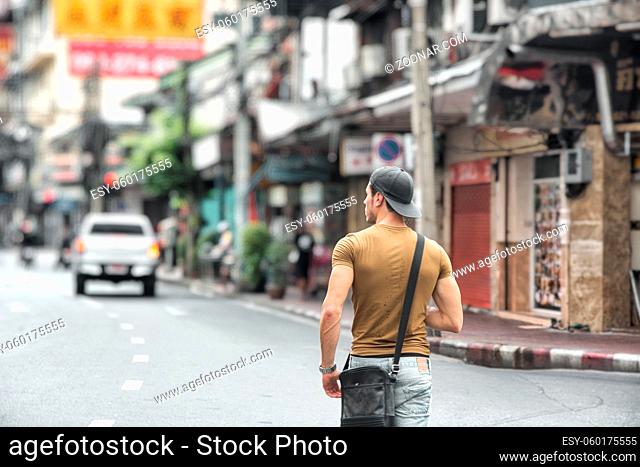 Back view of young fit man walking on busy sunny street in Bangkok, Thailand
