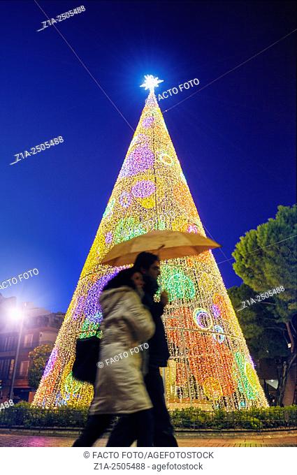 Couple with umbrellas passing by a Christmas tree. Getafe. Community of Madrid, Spain