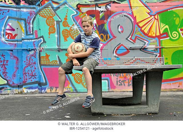 Nine-year-old boy sitting with his football at a table tennis table, kickabout area in Cologne, North Rhine-Westphalia, Germany, Europe