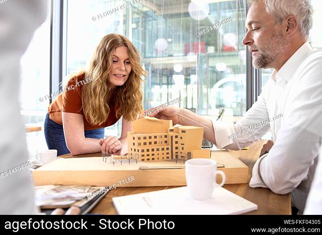 Male and female architects discussing over architectural model in office