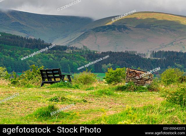 A bench and clouds over the Lake District in the background, seen at the Millom Ironworks Nature Reserve, Cumbria, England