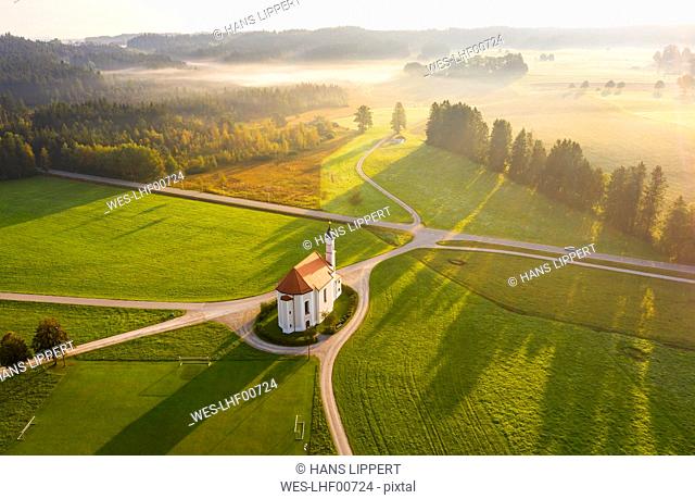 Germany, Bavaria, Dietramszell, Aerial view of countryside fields and Church of Saint Leonhard at foggy dawn