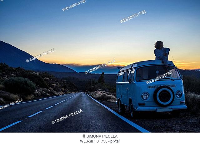 Spain, Tenerife, woman sitting on car roof of van parked at roadside