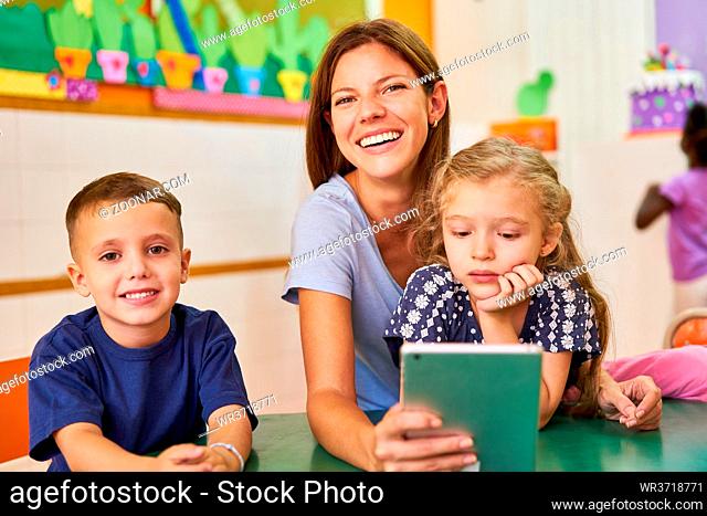 Fröhliche Kindergärtnerin und Kinder nutzen App auf dem Tablet Computer im Kindergarten