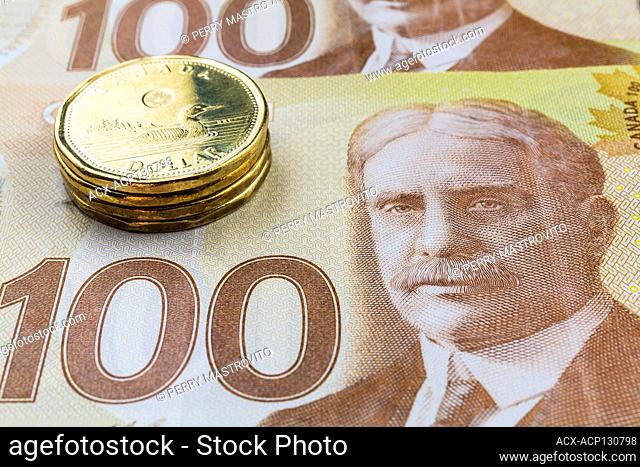 Stack of Canadian one-dollar coins on top of Canadian one-hundred dollar bank notes, Studio Composition, Quebec, Canada
