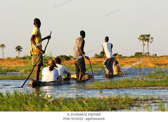 Kahnfahrer mit Touristen im traditionellen Mokoro Einbaum auf Exkursion im Okavango Delta, Botswana / Boatmen with tourists in traditional mokoro logboats on...