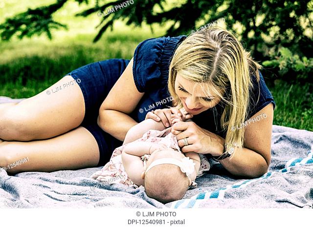 A young mother playing with her baby on a blanket in a city park on a warm summer day; Edmonton, Alberta, Canada