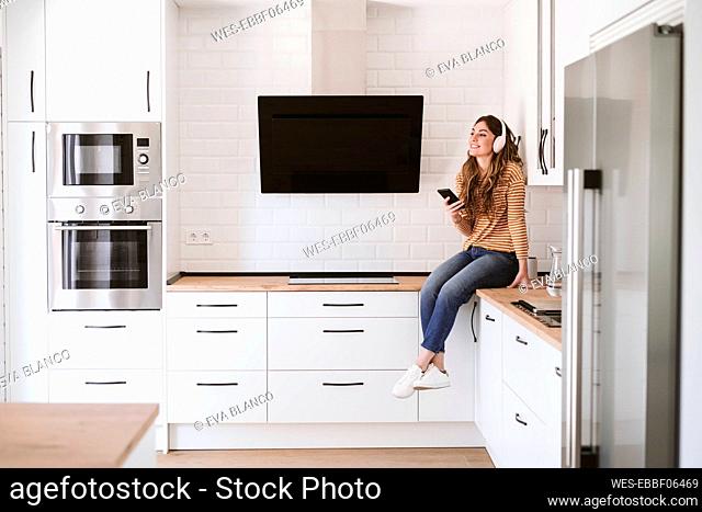 Young woman listening to music with headphones in kitchen at home