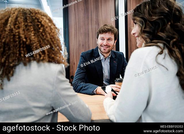 Smiling businessman with colleagues enjoying coffee break in office