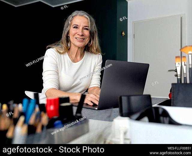 Smiling senior businesswoman sitting with laptop at workplace