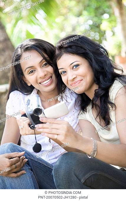 Portrait of two young women holding a digital video camera and smiling