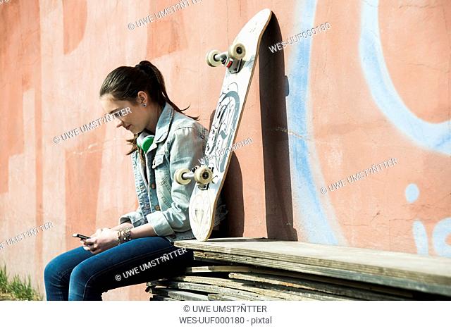 Teenage girl with skateboard using smartphone