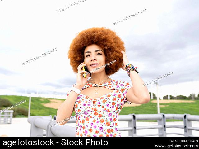 Woman with hand in hair talking on mobile phone at park