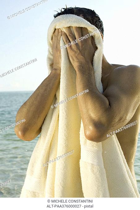 Man wiping face with towel, sea in background