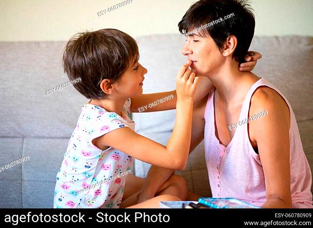 Happy mother and her little cute daughter doing make up for each other. Mum spending free time with her daughter