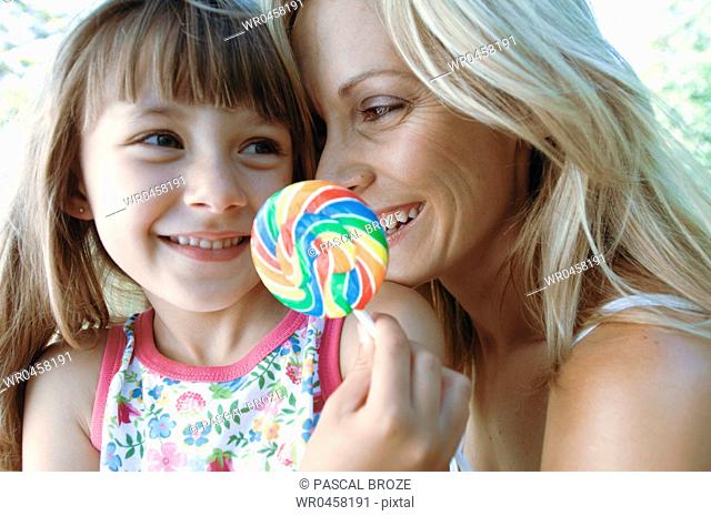 Close-up of a girl holding a lollipop with her mother and smiling