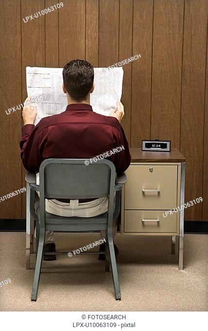 Back view of retro businessman sitting at desk reading paper