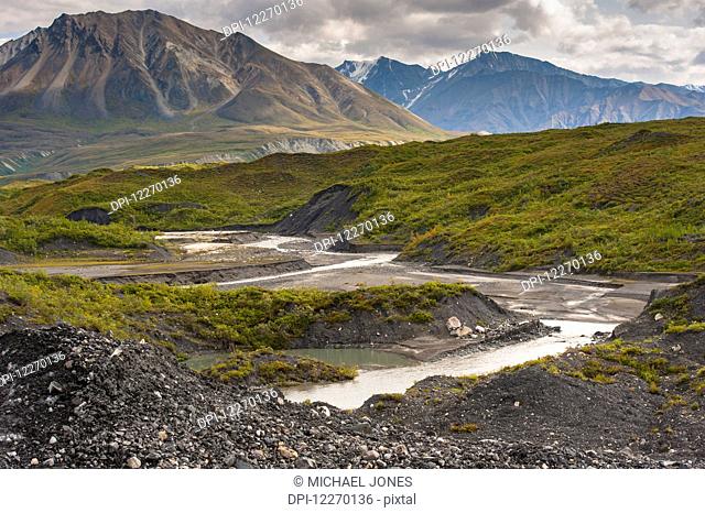 Thorofare River flowing next to the stone and vegatation covered Moldrow Glacier in Denali National Park and Preserve, Mount Eielson and the Alaska Range in the...