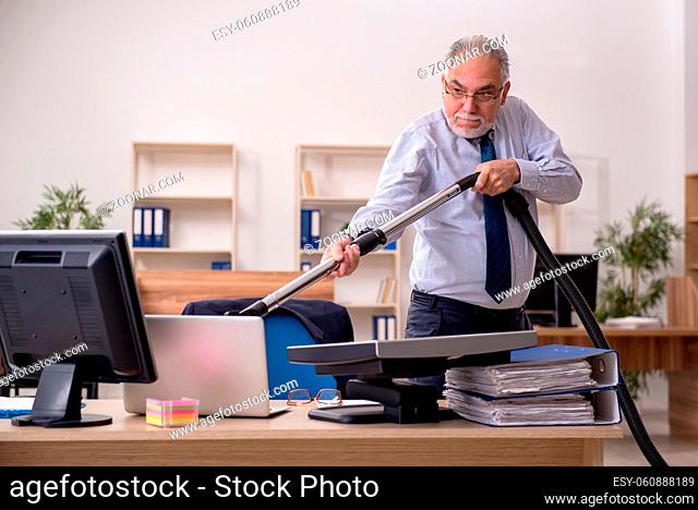 Old male employee holding vacuum cleaner at workplace