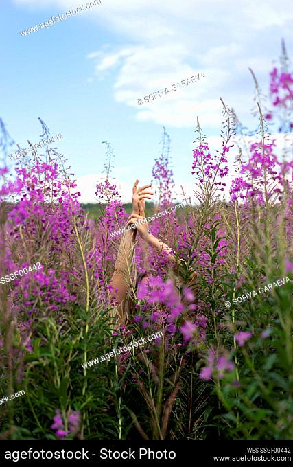 Woman with hand raised gesturing amidst pink flowering plants