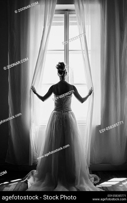 Shot of a beautiful young bride looking through a window on her wedding day. black and white vertical portrait photo
