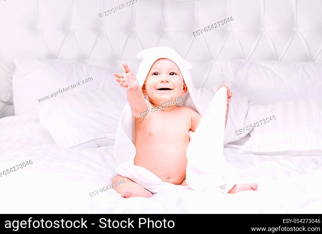 Adorable newborn baby boy with brown eyes sitting wrapped in a white towel with ears in light bed. A happy childhood and the concept of health