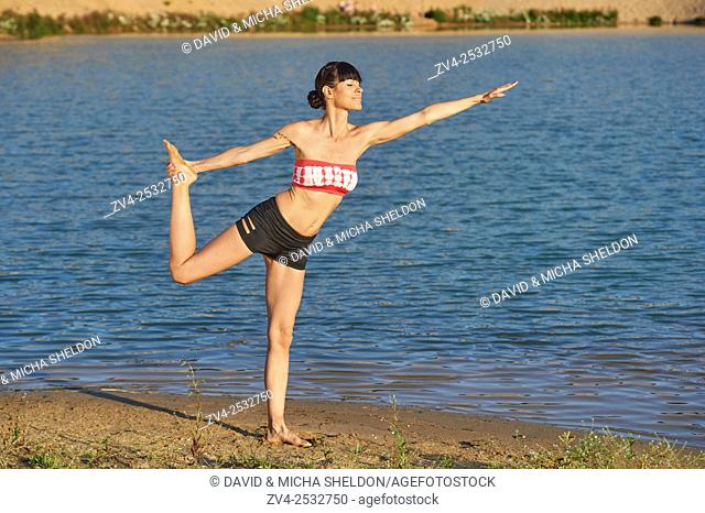 Young woman doing yoga on a beach next to a little lake