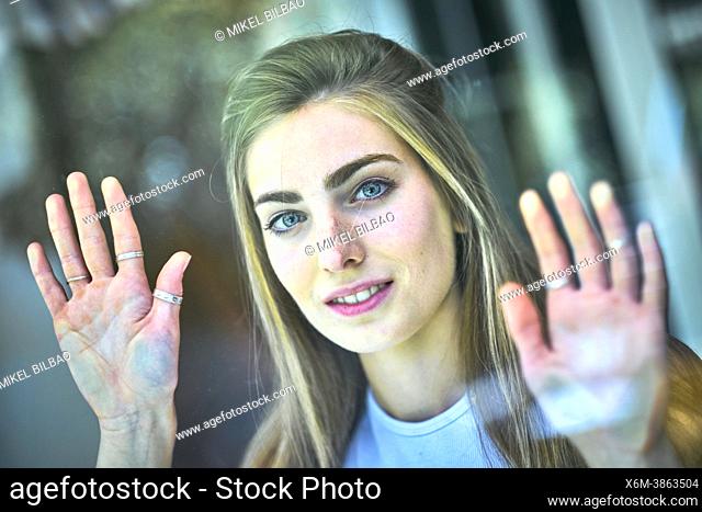 Portrait of a young beautiful caucasian woman in her 20's with long hair and blue eyes leaning with her hands on a glass. Lifestyle concept