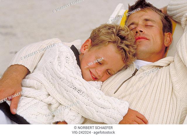 portrait, man and his 6 year-old blond son, both wearing bright pullover, sleep together on a relax-chair  - GERMANY, 08/08/2004