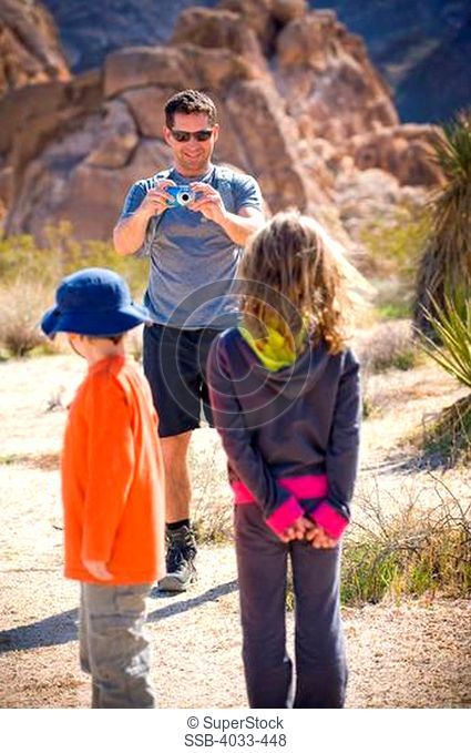Mid adult man taking a picture of his children, Joshua Tree National Monument, California, USA