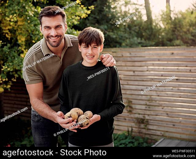 Father and son standing in garden holding freshly hervested poatoes
