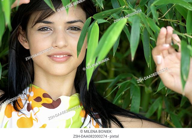 Young woman smiling amongst bamboo foliage, portrait