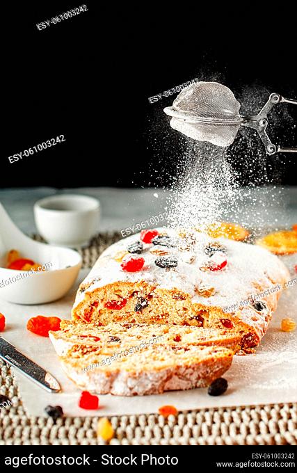 Holiday baking. Christmas cake coated with powdered sugar. Close up hands of the chef with metal sieve sprinkling cake with Powdered sugar at pastry shop...