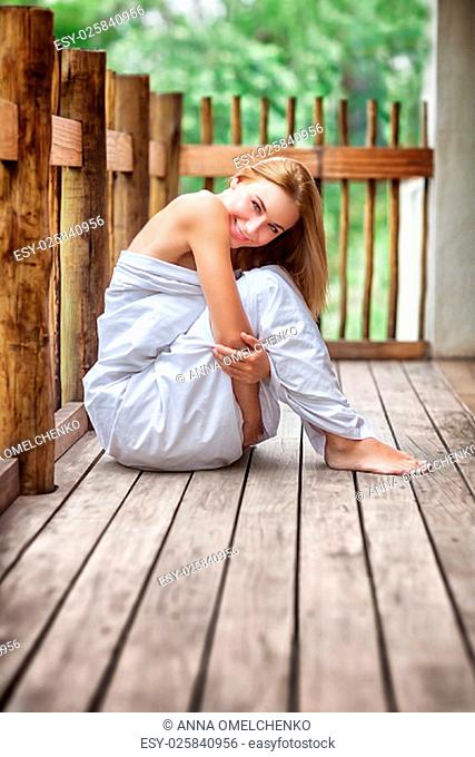 Gentle woman wrapped in the bed sheet sitting on the terrace, spending peaceful morning in spa hotel, relaxing outdoor and enjoying life
