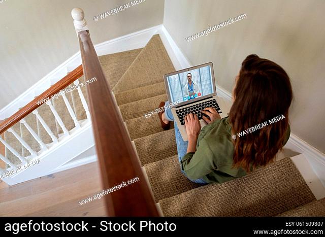Woman having a video meeting on her laptop while sitting on staircase