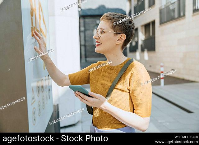 Mid adult woman reading map while holding smart phone standing in city on sunny day