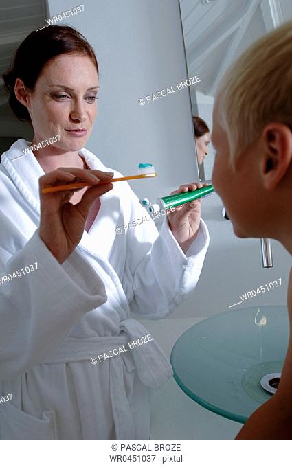Mid adult woman giving toothbrush to her son