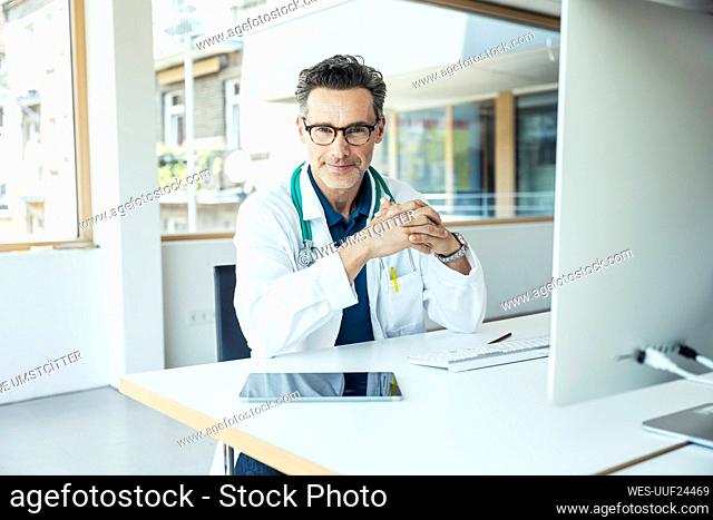 Male professional with hands clasped sitting at desk