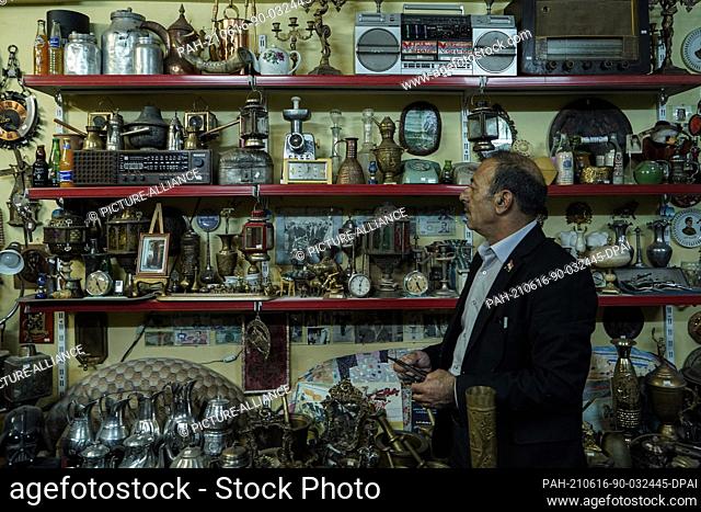 16 June 2021, Iraq, Mosul: Iraqi Fakhri Suleiman Al-Tai stands at his house next to a shelf packed with antique pieces that he collected after he returned to...