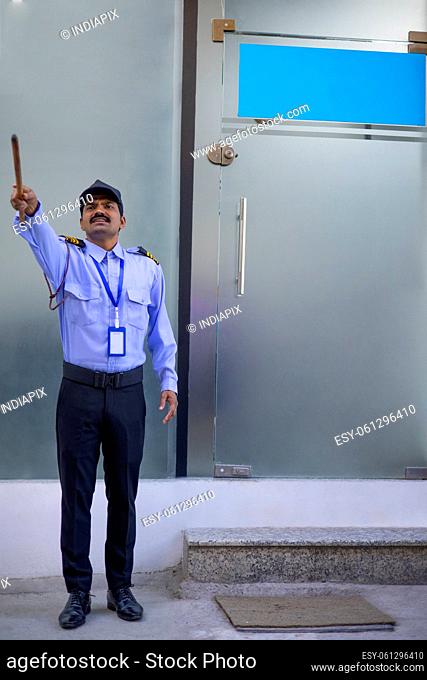 Security guard pointing away with stick while working in front of gate