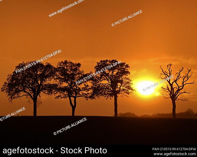 15 May 2021, Brandenburg, Sieversdorf: Colorful shines the sunset over the landscape. The atmosphere is dramatic because the light of the sun is obscured by...